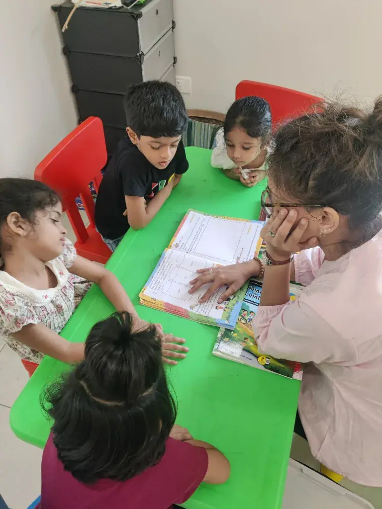A teacher reading with four children at a small table at ULTRA_school, Jawahar Nagar